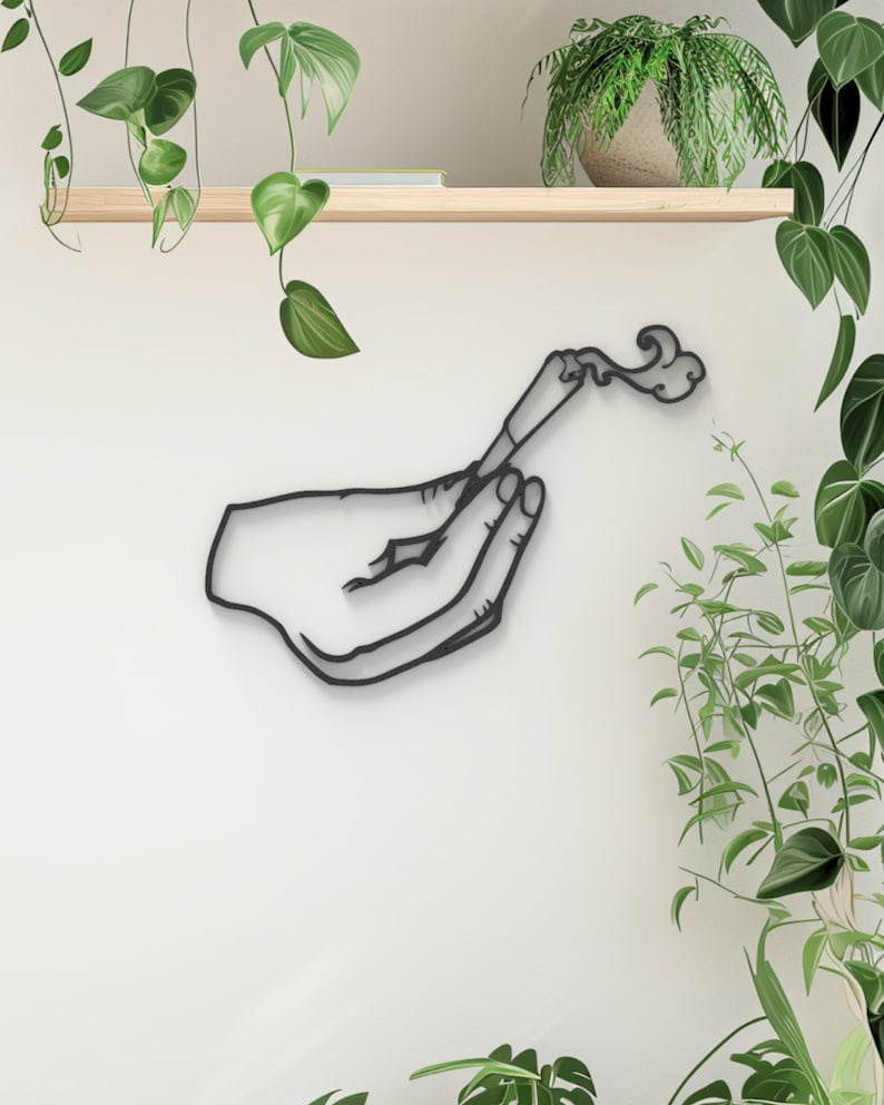 May include: Black metal wall art sculpture of a hand holding a lit stick of incense with smoke rising from the end.