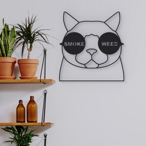 Pode incluir: Arte de parede de metal preto de um gato usando &oacute;culos de sol com as palavras "SMOKE" e "WEED" nas lentes.