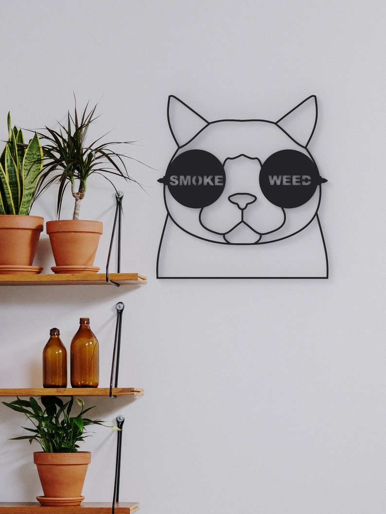 Pode incluir: Arte de parede de metal preto de um gato usando &oacute;culos de sol com as palavras "SMOKE" e "WEED" nas lentes.