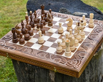Könnte beinhalten: Ein Schachspiel aus Holz mit aufwendigen Schnitzereien auf dem Brett und den Figuren. Das Brett ist geöffnet und die Figuren sind in einem laufenden Spiel angeordnet. Das Brett ist braun mit einem weißen und braunen Schachbrettmuster. Die Figuren sind aus hellem und dunklem Holz.