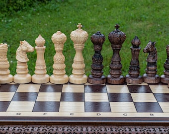 Puede incluir: Un juego de ajedrez de madera con piezas de color marrón claro y oscuro dispuestas en un tablero de ajedrez. Las piezas están talladas con intrincados detalles y el tablero tiene un acabado de madera clara.