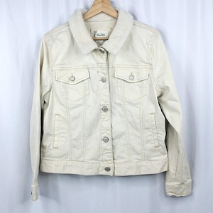 May include: A cream-colored denim jacket featuring a white sherpa collar, long sleeves, and a front button closure. The jacket includes two chest pockets with button flaps and two side slit pockets. A Mudd brand label is visible at the neckline.