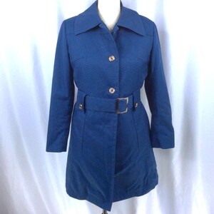 May include: A solid blue trench coat featuring a wide collar, long sleeves, and a front button closure. The coat includes a matching fabric belt with a rectangular silver-toned buckle at the waist, providing a structured fit and a clean finish.