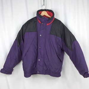 Könnte beinhalten: Eine vintage Winterjacke in Lila und Schwarz mit rotem Innenfutter. Die Jacke hat einen hohen Kragen, Druckknöpfe sowie einen gerippten Saum und Bündchen. Die Schultern sind schwarz, und die Jacke hängt vor einem weißen Hintergrund.