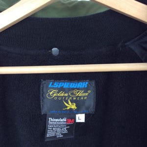 Może przedstawiać: Czarna kurtka z podszewką z czarnego polaru i etykietą z napisem "ISPIEWAK Golden Fleece OUTERWEAR" z logo ptaka i tekstem "Thinsulate 3M Thermal Insulation" oraz etykietą rozmiaru z napisem "L".