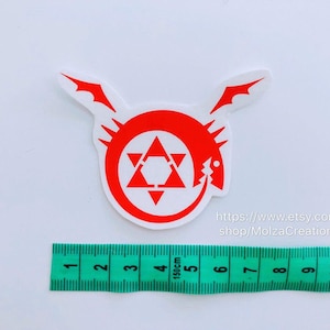 May include: Red and white vinyl sticker of the Fullmetal Alchemist symbol, a circle with a star inside and a dragon head on the side. The sticker is 5 cm in diameter and is on a white background.