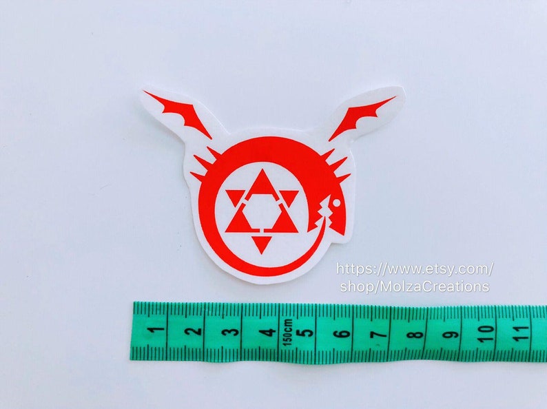 May include: Red and white vinyl sticker of the Fullmetal Alchemist symbol, a circle with a star inside and a dragon head on the side. The sticker is 5 cm in diameter and is on a white background.