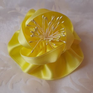 Könnte beinhalten: Eine gelbe Satinbandblume mit einer Mitte aus weißen und silbernen Perlen.