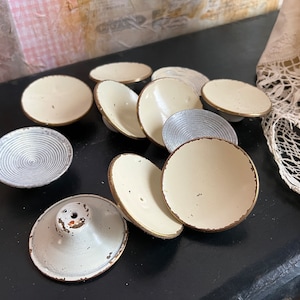 Pode incluir: Uma coleção de dez tigelas pequenas de cerâmica branca com um design decorativo de círculos concêntricos em relevo. As tigelas estão dispostas em semicírculo sobre uma superfície preta.