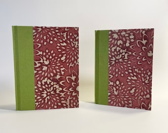 May include: Two burgundy journals with a green spine and a white floral pattern on the front cover.