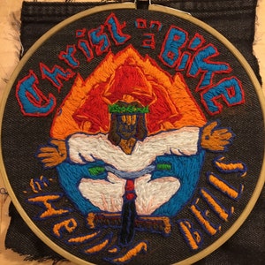 Könnte beinhalten: Gestickter Aufnäher mit schwarzem Hintergrund, der eine Figur von Jesus auf einem Fahrrad zeigt, mit den Worten "Christ's Bike" darüber und "Hell's Bells" darunter.