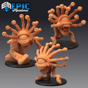 May include: Three 3D printed miniature figures of a beholder creature with a single large eye and multiple tentacles. The figures are painted in a light brown color.