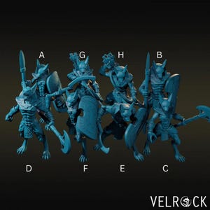 Può includere: Una collezione di otto figurine in miniatura color teal ispirate ad Anubi, ciascuna in una posa dinamica e con varie armi e scudi. Le figurine sono etichettate dalla A alla H. Il logo Velrock è visibile in basso a destra.