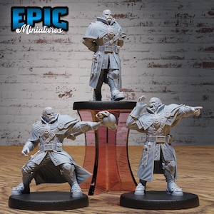 May include: Three gray painted miniature figures of people wearing long coats and hats. The figures are standing on black bases. The figures are on a wooden surface. The text "EPIC Miniatures" is in the upper left corner of the image.
