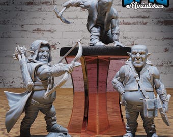 Może przedstawiać: Trzy szare, pomalowane miniaturowe figurki goblinów. Jeden goblin trzyma kilof, drugi łuk i strzałę, a trzeci torbę i tarczę. Gobliny stoją na drewnianej powierzchni z ceglaną ścianą w tle. Tekst "EPIC Miniatures" jest widoczny w prawym górnym rogu obrazu.