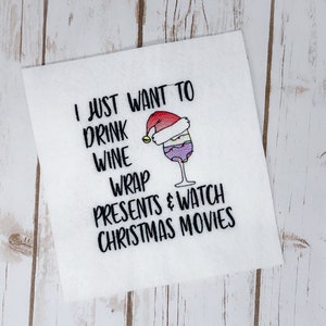 May include: White embroidery design on a white fabric background. The design says "I just want to drink wine wrap presents & watch Christmas movies". A wine glass with a Santa hat on top is in the design.