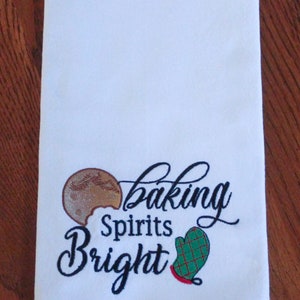 May include: White kitchen towel with a red, green, yellow, and blue plaid border. The towel has black embroidery that reads "baking spirits bright" with a gingerbread cookie and a green oven mitt.