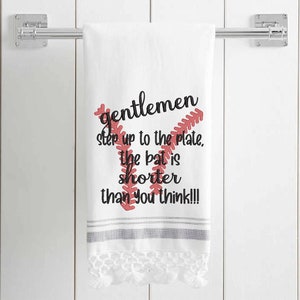 May include: White kitchen towel with red embroidered baseball stitching and the text "gentlemen step up to the plate, the bat is shorter than you think!!!"