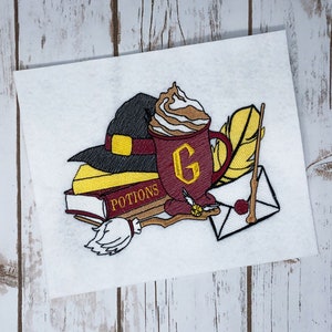 May include: Embroidered design featuring a black witch's hat, a maroon mug with a 'G', a stack of books with 'POTIONS' text, a broom, a feather, and an envelope with a wand. The design is on a white background.