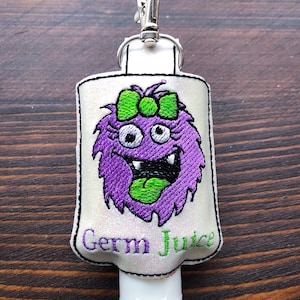 May include: A white hand sanitizer holder with a purple monster with green hair and a bow, and the text "Germ Juice".