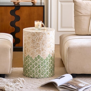 May include: A decorative side table with a floral and leaf design. The top half has a cream floral pattern, with a green leaf pattern on the bottom. A lit candle sits on top. The table is surrounded by cream-colored furniture. The table is approximately 40 cm in diameter.