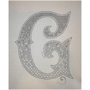 Könnte beinhalten: Ein schwarzes und weißes Kreuzstich-Design des Buchstabens G auf einem beigefarbenen Stoffhintergrund.