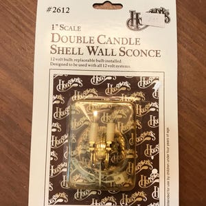 May include: A gold-colored double candle shell wall sconce, 1-inch scale, in a clear plastic package. The packaging includes the text "Double Candle Shell Wall Sconce" and "Helping you reach your vision."