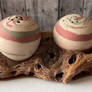 May include: A set of two salt and pepper shakers with a swirl design in shades of brown, pink, and green. The shakers are sitting on a wooden base.