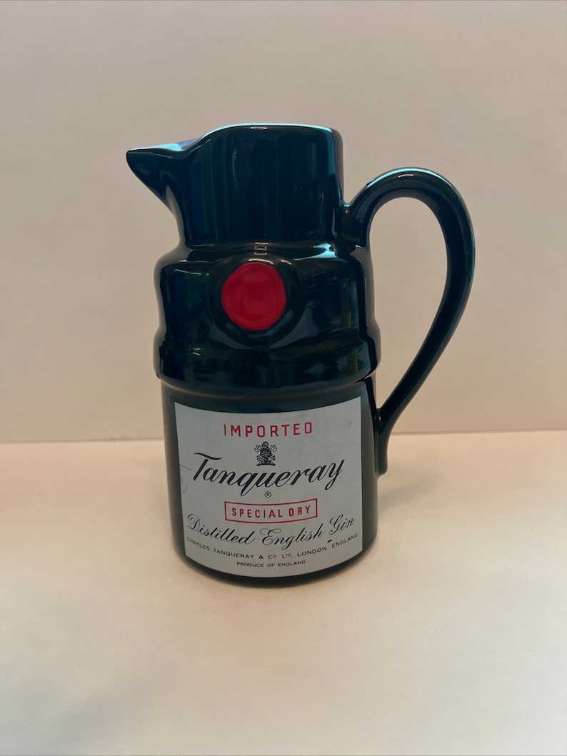 Op de afbeelding: Zwarte keramische kan in de vorm van een Tanqueray-ginfles. De kan heeft een rode dop en het etiket vermeldt "IMPORTED Tanqueray SPECIAL DRY Distilled English Gin CHARLES TANQUERAY & CO LTD LONDON ENGLAND PRODUCE OF ENGLAND"