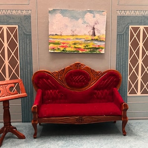 May include: Miniature dollhouse living room scene with a red velvet sofa, a wooden music stand, and a painting of windmills. The walls are painted in shades of blue and gray, creating a classic interior design.