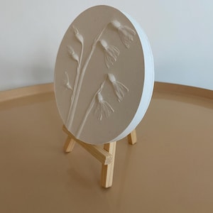 May include: A white circular plaster relief sculpture of a cluster of delicate white flowers on a small wooden easel.