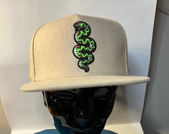 May include: A beige baseball cap with a green and black snake embroidered on the front.