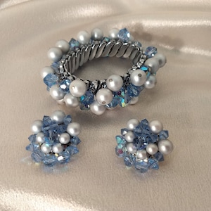 May include: A set of blue and white pearl jewelry featuring a bracelet and a pair of earrings. The bracelet is made of a silver metal band with blue and white pearls attached. The earrings are round and feature blue and white pearls.