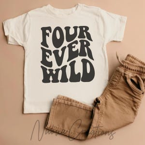 Pode incluir: Camiseta creme para criança com as palavras "FOUR EVER WILD" em letras pretas e arrojadas, em estilo retrô. Combinada com calças marrons. A roupa é exibida em um fundo neutro.
