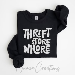 May include: Black long-sleeve sweatshirt with the white text "THRIFT STORE WHORE" in a bold, retro font. The sweatshirt has a crew neck and cuffed sleeves. The brand name "Nuova Creations" is written in cursive at the bottom.