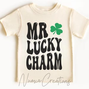 Puede incluir: Una camiseta blanca con texto negro que dice "Mr. Lucky Charm" y un trébol verde.
