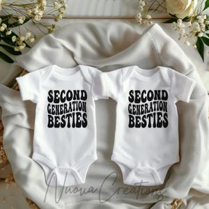 May include: Two white baby onesies with black text that reads "Second Generation Besties".