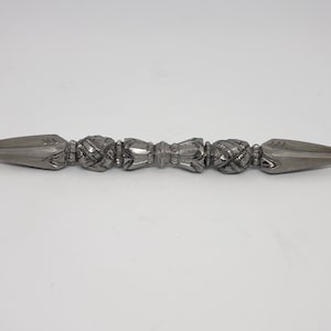 May include: A silver metal throwing weapon with a double-pointed tip and decorative details. The weapon is made of metal and has a textured surface.