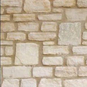 May include: A wall made of light beige and cream colored stones with a rough texture. The stones are arranged in a random pattern and are held together with a light brown mortar.