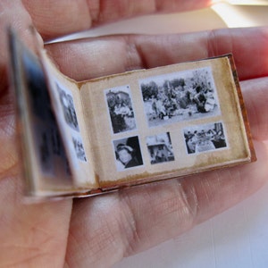 May include: A small, brown photo album with black and white photos of people. The album is open to reveal several photos, including a group of people standing together, a woman in a hat, and a group of people sitting at a table.