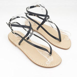 May include: Black leather sandals with criss-cross straps and a buckle closure. The sandals have a flat sole and a toe loop.