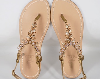 May include: Gold leather sandals with a jeweled strap featuring a leaf design. The sandals have a brand label that reads "SORRENTO  SYRENIA".