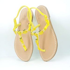 Op de afbeelding: Gele leren sandalen met een delicaat ananasontwerp. De sandalen hebben een dunne band die om de enkel gaat en een gespsluiting. De sandalen zijn gemaakt van hoogwaardig leer en perfect voor de zomer.