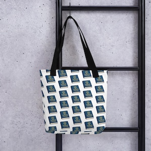 May include: White tote bag with a repeating pattern of blue books with gold lettering. The books are labeled "THE BOOK OF MORMON". The bag has black handles and is hanging on a black metal bar.