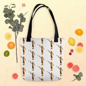 May include: White tote bag with a repeating pattern of a gold-colored statue blowing a horn. The bag has black handles. The background is a light yellow color with fruit and a sprig of greenery.