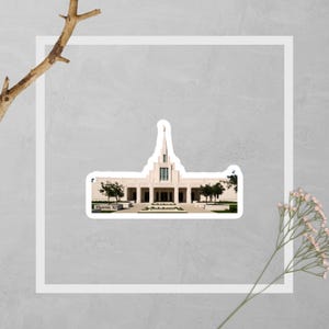May include: A sticker featuring a white building with a tall spire, trees, and the text "Phoenix Az." The building has a symmetrical design with columns and a central entrance. The sticker is set against a white border and a gray background.
