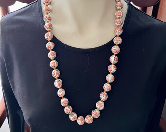 Puede incluir: Un collar de cuentas de porcelana blanca con diseños florales rojos y verdes y acentos naranjas. Las cuentas son redondas y tienen un carácter chino tradicional impreso.