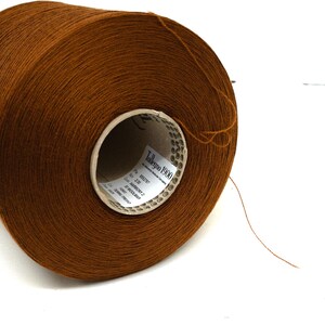 May include: A large spool of brown yarn, ideal for knitting or crochet projects. The yarn is tightly wound and has a smooth texture. The label on the spool reads "Tollegno 1900".