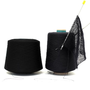 Könnte beinhalten: Zwei Spulen mit schwarzem Garn, eine mit einem gestrickten Schal darüber gelegt.