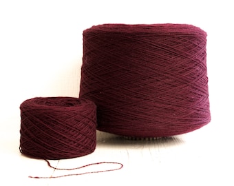 May include: Two spools of maroon yarn, one larger than the other, are shown on a white surface. The yarn is wound tightly and has a smooth texture.